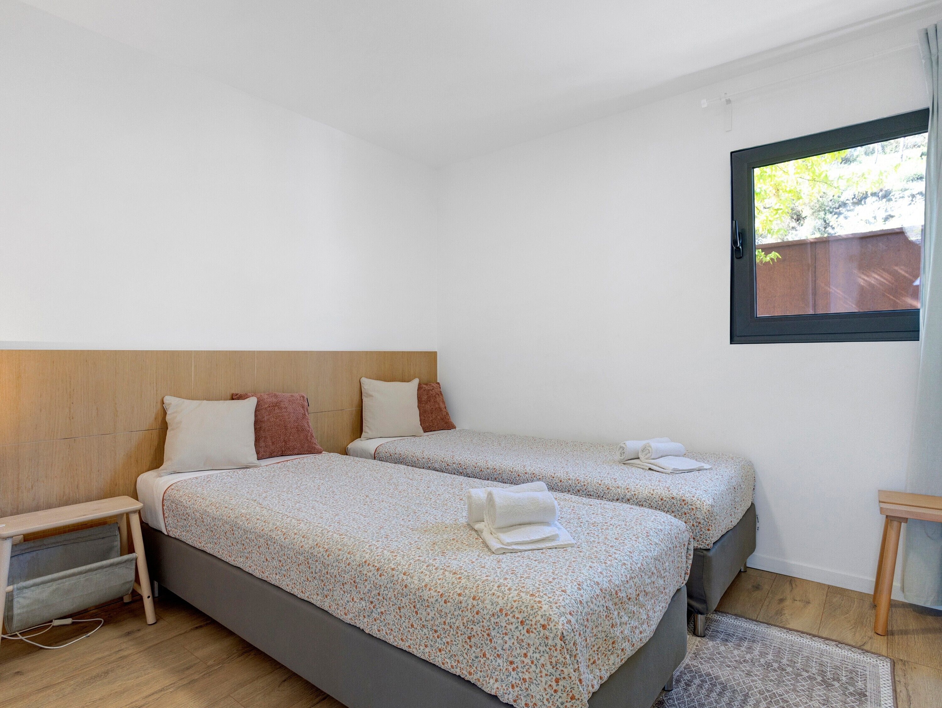 Een slaapkamer met twee bedden, een houten hoofdbord, een nachtkastje en een raam met uitzicht.