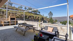 An outdoor patio with a stone table, wooden bench, wicker furniture, and a stone fireplace. - Holiday Home 'Casa Dona Florinda - Ermida, Pnpg' with Shared Pool, Shared Garden and Wi-Fi (Ermida)