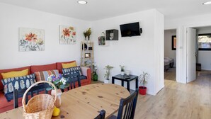 A modern living room with a sofa, a dining table, and a TV mounted on the wall. - Holiday Home 'Casa Dona Florinda - Ermida, Pnpg' with Shared Pool, Shared Garden and Wi-Fi (Ermida)