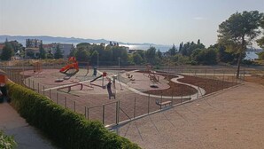 Un parque infantil con diverso equipo de juegos, rodeado por una zona pavimentada y una valla.