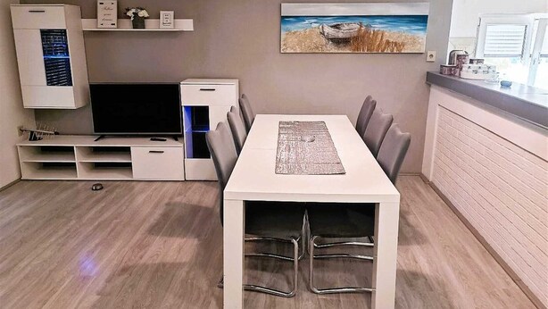 Un espacio habitable moderno y funcional con mesa, sillas, televisión de pantalla plana y zona de cocina.