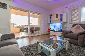 Een woonkamer met een glazen salontafel, een bank, een televisie en een schuifpui die leidt naar een balkon.