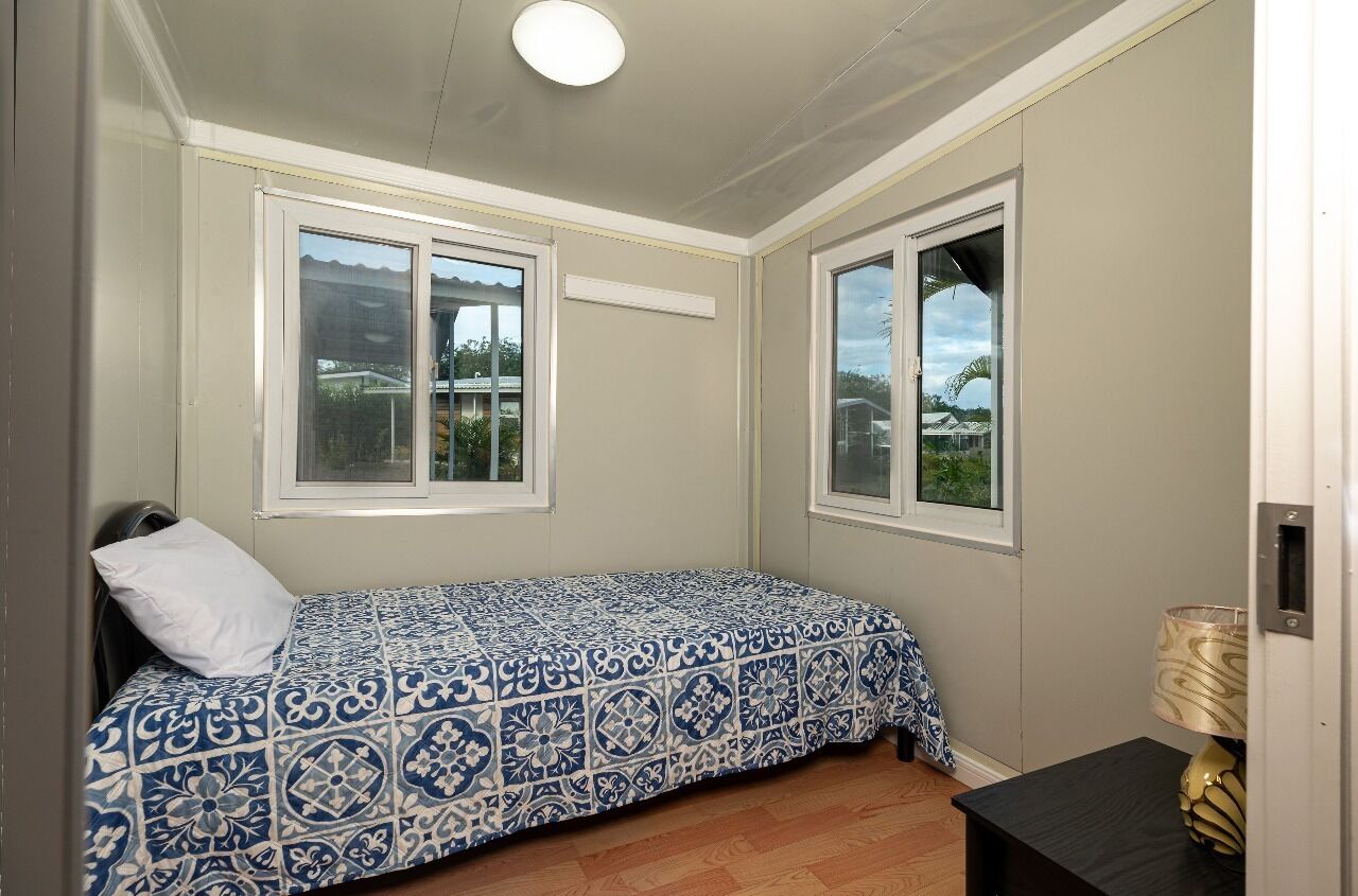 A small bedroom with a single bed, two windows, a bedside table, and a lamp.