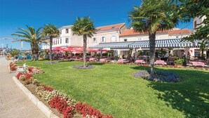 Ein sonniger Außenbereich eines Cafés mit Tischen, Stühlen, Palmen und einem Gebäude mit rotem Dach.