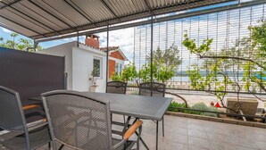 Eine überdachte Terrasse mit Tisch und Stühlen, Meerblick und ein kleiner Garten mit Pflanzen.
