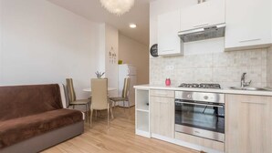Eine moderne Küche mit weißen Schränken, einem Gasherd und einem Backofen. Ein Essbereich mit Tisch und Stühlen ist ebenfalls vorhanden.