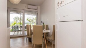 Eine moderne Küche mit einem weißen Kühlschrank, einem Essbereich mit vier Stühlen und einem großen Fenster mit Blick ins Freie.