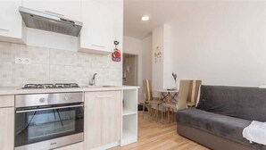 A compact kitchen with a stove, oven, and sink. There is a dining area with a table and chairs, and a gray sofa in the living space. - Studio apartment Pebble 3 (Turanj)