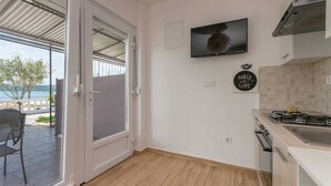 A modern kitchen with a TV, a sign saying "Baked with Love", and a view of the sea through a glass door. - Studio apartment Pebble 3 (Turanj)