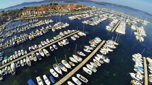 Eine Luftaufnahme einer Marina mit zahlreichen Booten, die kreisförmig vor Anker liegen, umgeben von einer Küstenstadt mit Gebäuden und blauem Himmel.