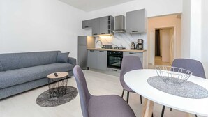 Ein modernes Wohnzimmer mit einem grauen Sofa, einem runden Couchtisch und einem Essbereich mit weißem Tisch und grauen Stühlen.
