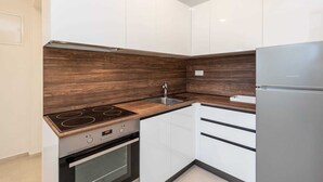 Une cuisine moderne avec des meubles blancs, un pare-feu en bois, un évier en acier inoxydable et un four encastré.