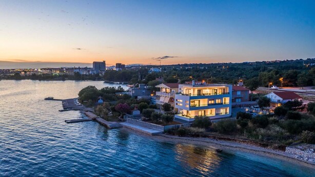 Un immeuble moderne à plusieurs étages, doté de balcons, situé au bord de l’eau, avec un quai et des bateaux.