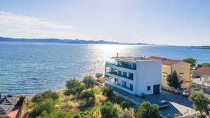 Un bâtiment moderne doté d’une piscine donnant sur une mer calme, entouré de verdure et d’autres immeubles résidentiels.