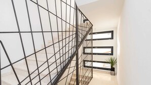 Eine moderne Treppe mit Metallgeländer, die zu einer Zwischenebene mit großen Fenstern und einem Blumentopf führt.