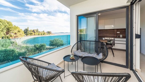 Ein Balkon mit Blick auf das Meer, zwei Stühle, ein kleiner Tisch und eine Küchenzeile.