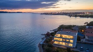 Una casa moderna de dos pisos con un balcón que da a un cuerpo de agua tranquilo, junto a un muelle.