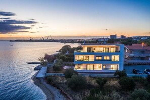 A modern two-story building with multiple balconies overlooking a waterfront. - Beachfront Villa Fresca (F4) Penthouse 6+1 guests (Bibinje)