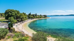 A coastal beach with clear turquoise waters, a sandy shoreline, and a row of beach umbrellas. - Beachfront Villa Fresca (F4) Penthouse 6+1 guests (Bibinje)
