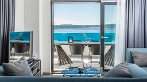 A modern room with a glass door leading to a balcony with a table and chairs, overlooking a body of water and distant hills. - Beachfront Villa Fresca (F4) Penthouse 6+1 guests (Bibinje)