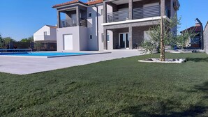 Una casa moderna de dos pisos con piscina, césped cuidado y un pequeño árbol en el jardín delantero.