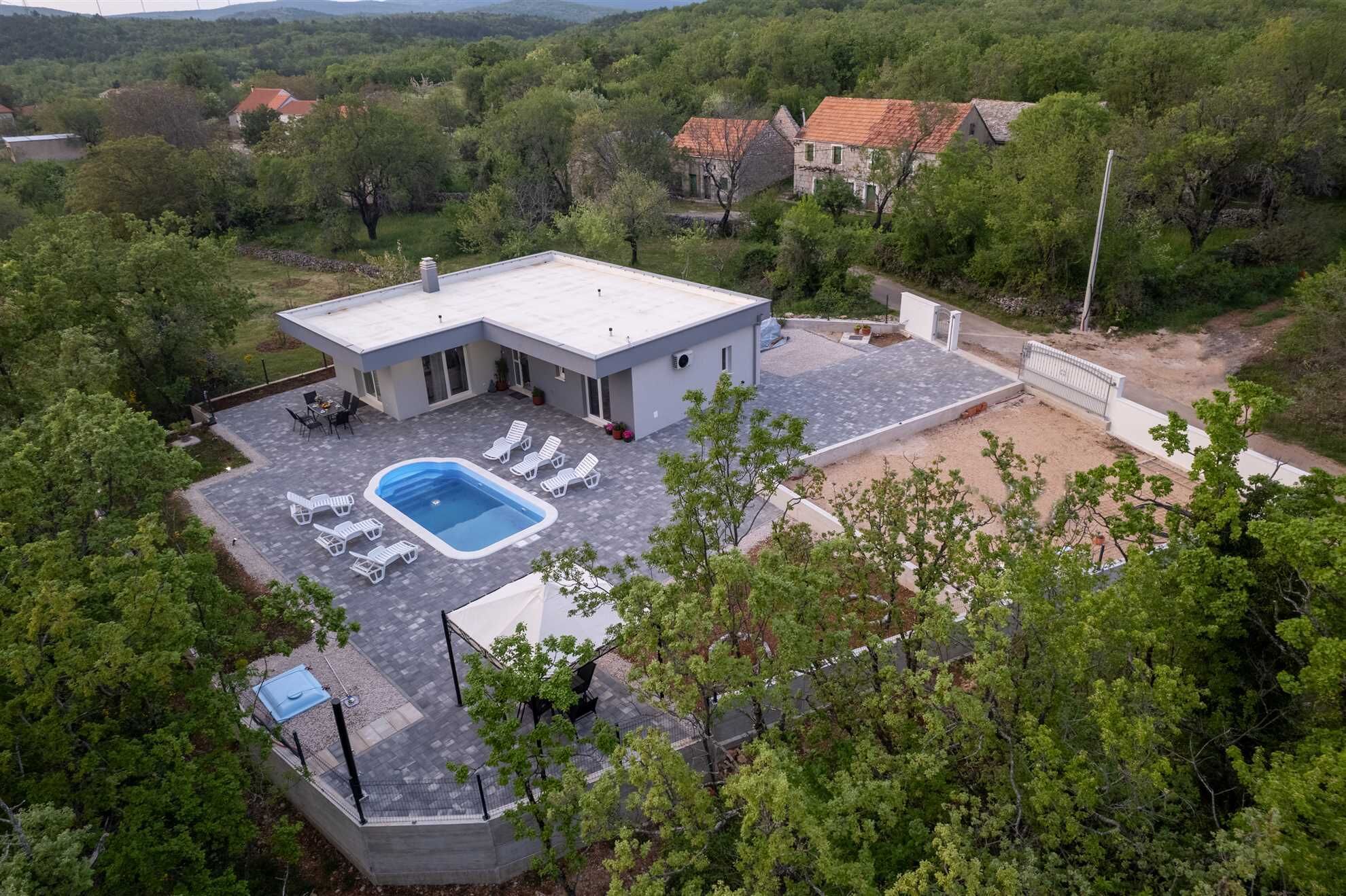 Ein modernes Haus mit Pool auf dem Dach, umgeben von üppiger Vegetation und sanften Hügeln im Hintergrund.