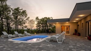 Un área de piscina moderna al aire libre con sillones de descanso y una terraza.