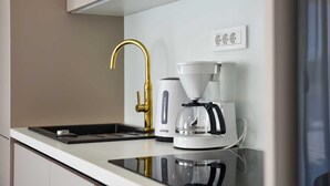 Una cocina moderna con un grifo dorado, una cafetera blanca y una hornilla negra.