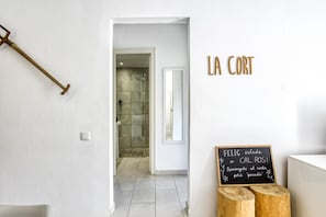 Un pasillo con ducha, un taburete de madera y una pizarra con texto.