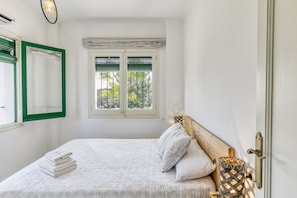 Un dormitorio con una cama, una ventana con persianas, una puerta y una lámpara fijada a la pared.