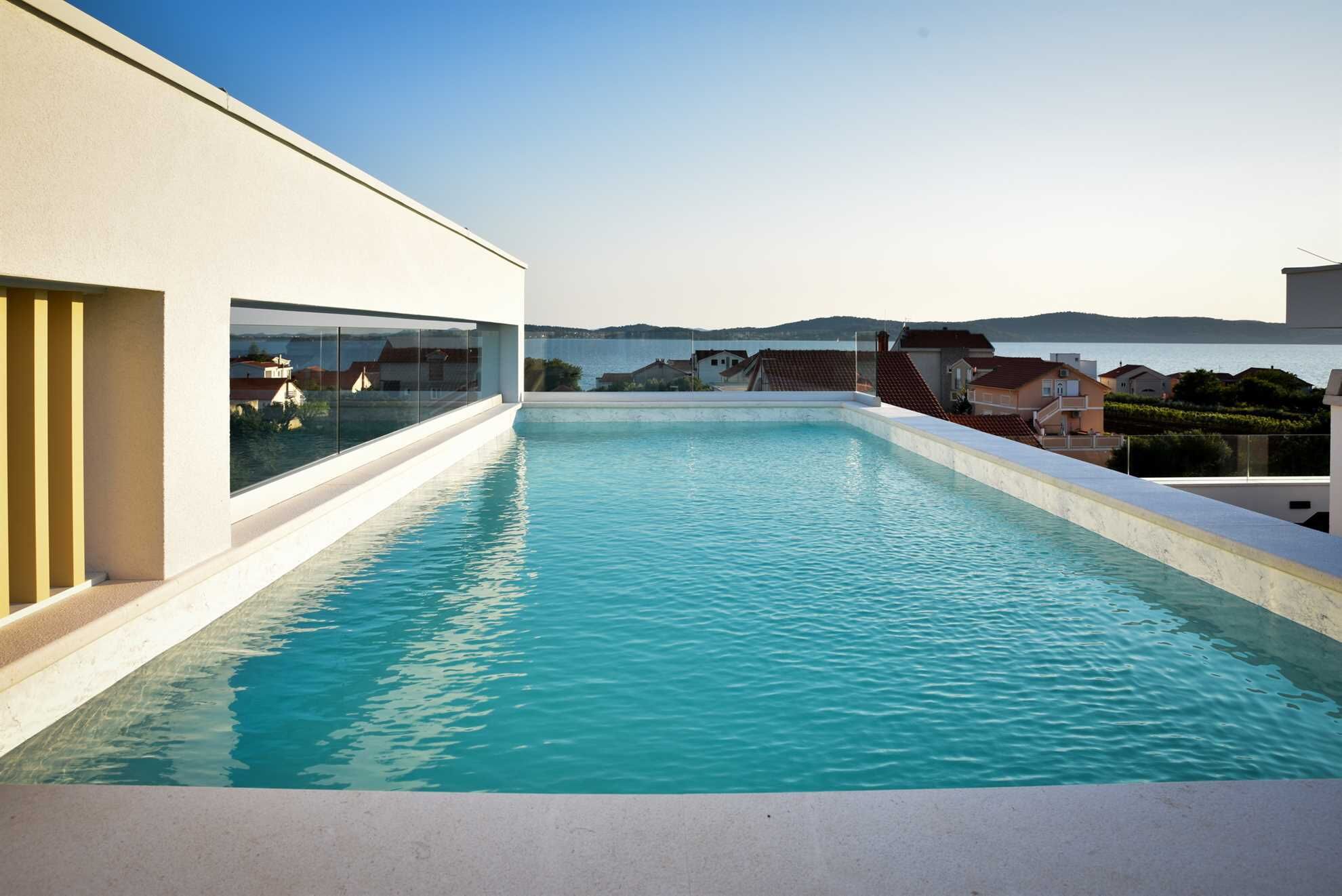 A modern infinity pool with a clear view of the sea and surrounding buildings.