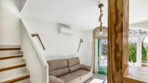Een trap leidt naar een woonruimte met een bank, een hanglamp en uitzicht door een glazen deur.