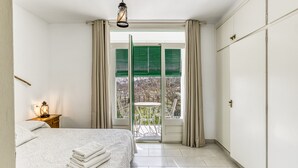 Een slaapkamer met een bed, een nachtkastje met een lamp, een balkon met een tafel en stoelen, en een schuifpui.