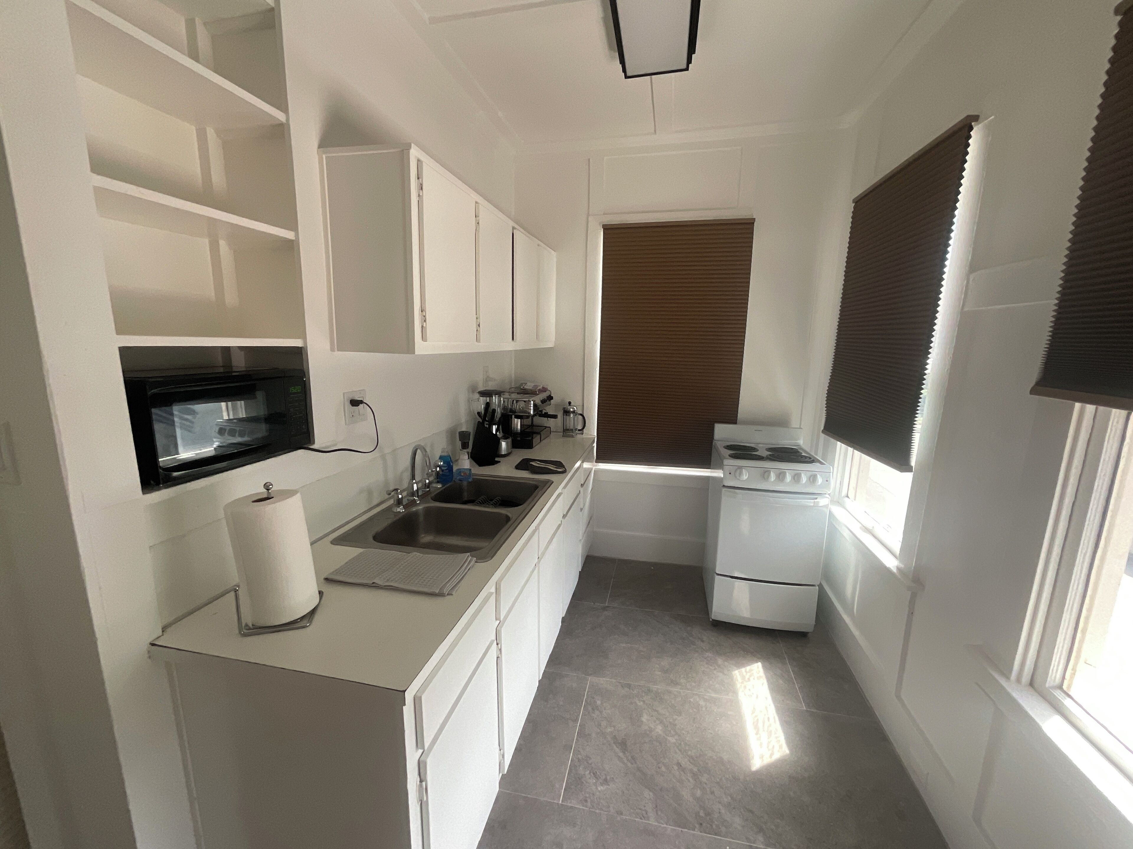 Una cocina compacta con armarios blancos, un lavamanos de acero inoxidable, una estufa y un microondas.