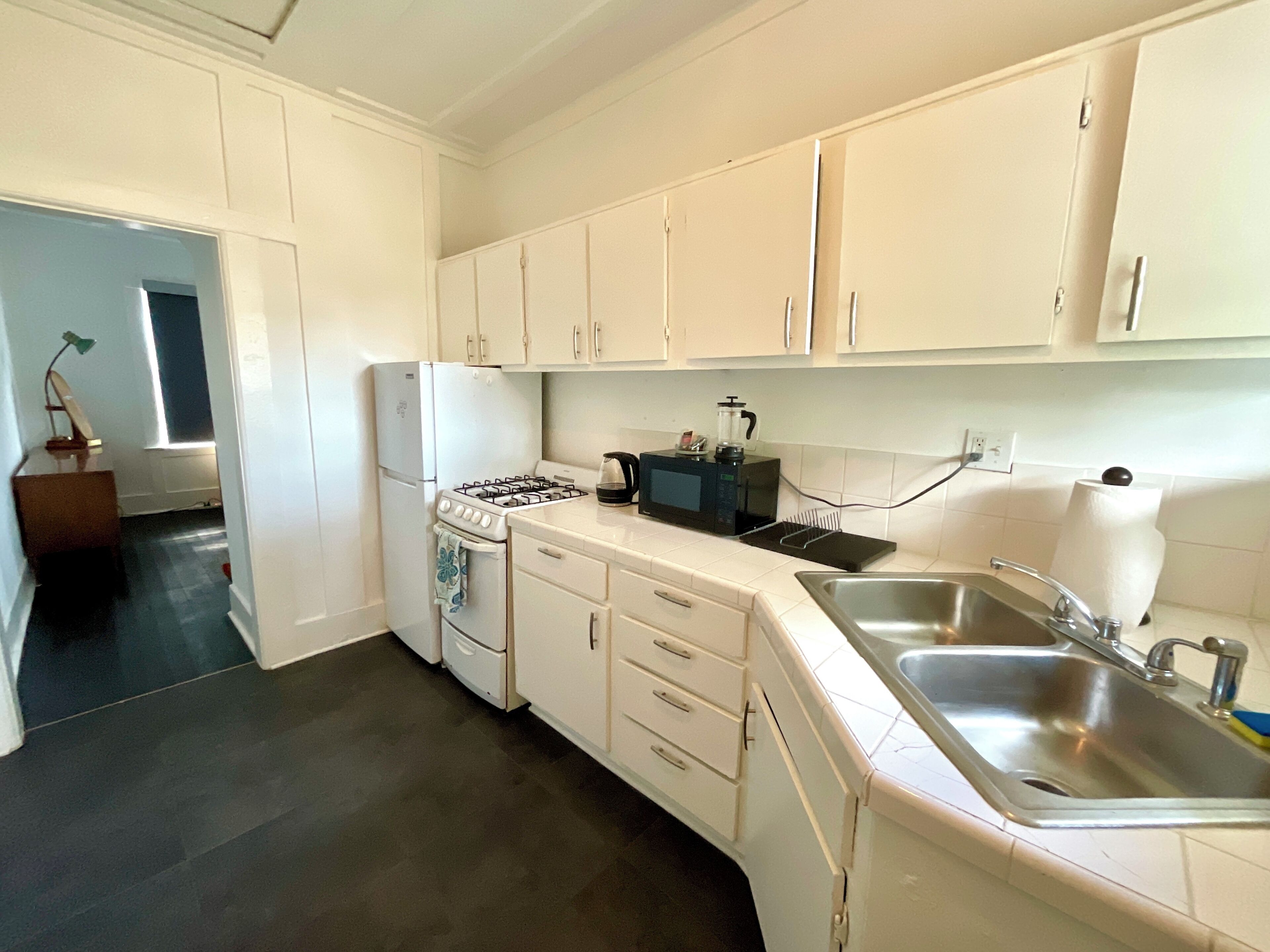 A kitchen with white cabinets, a stove, a microwave, and a sink.