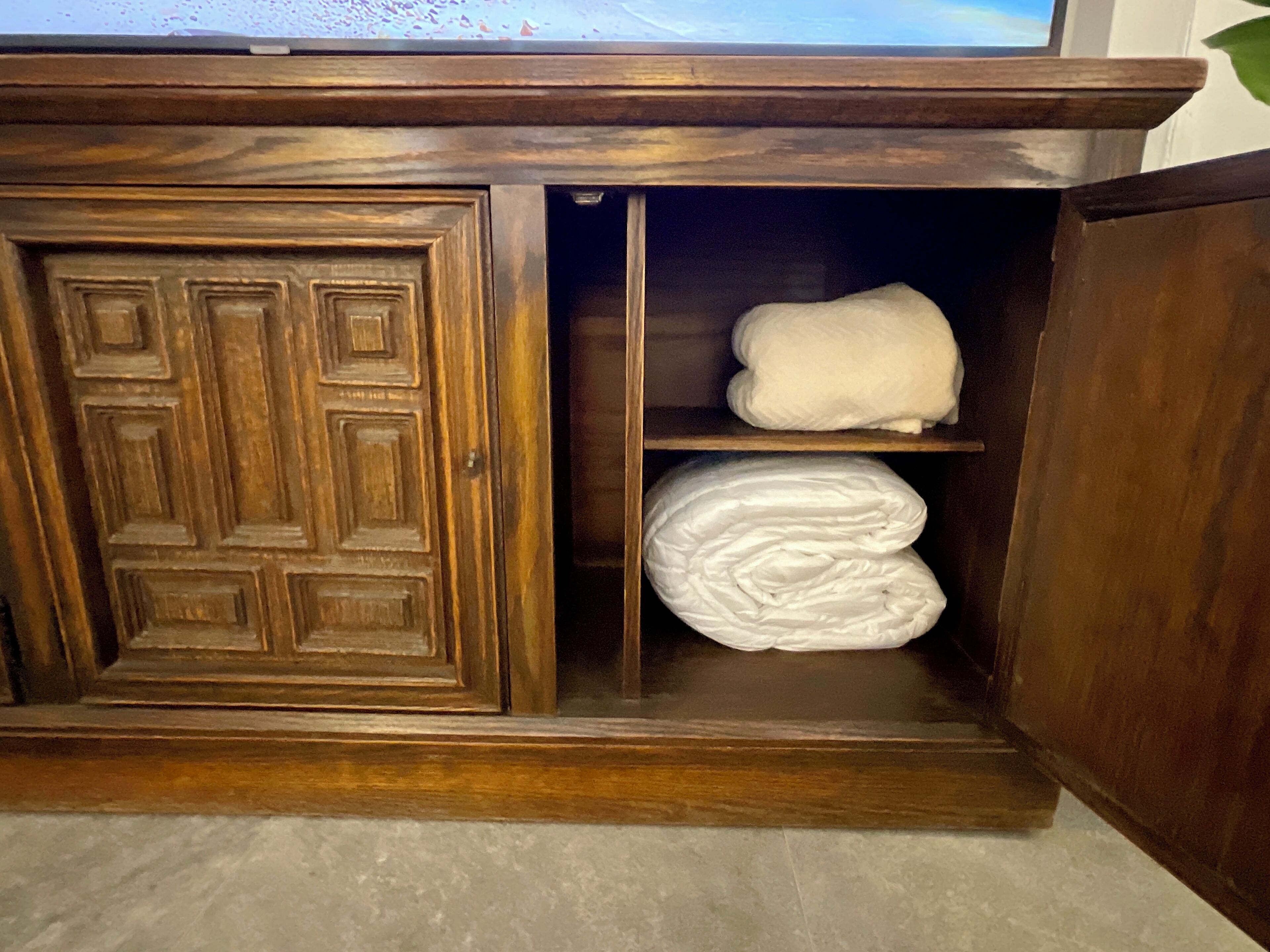 A wooden cabinet with a door and two shelves, one of which holds folded white towels.