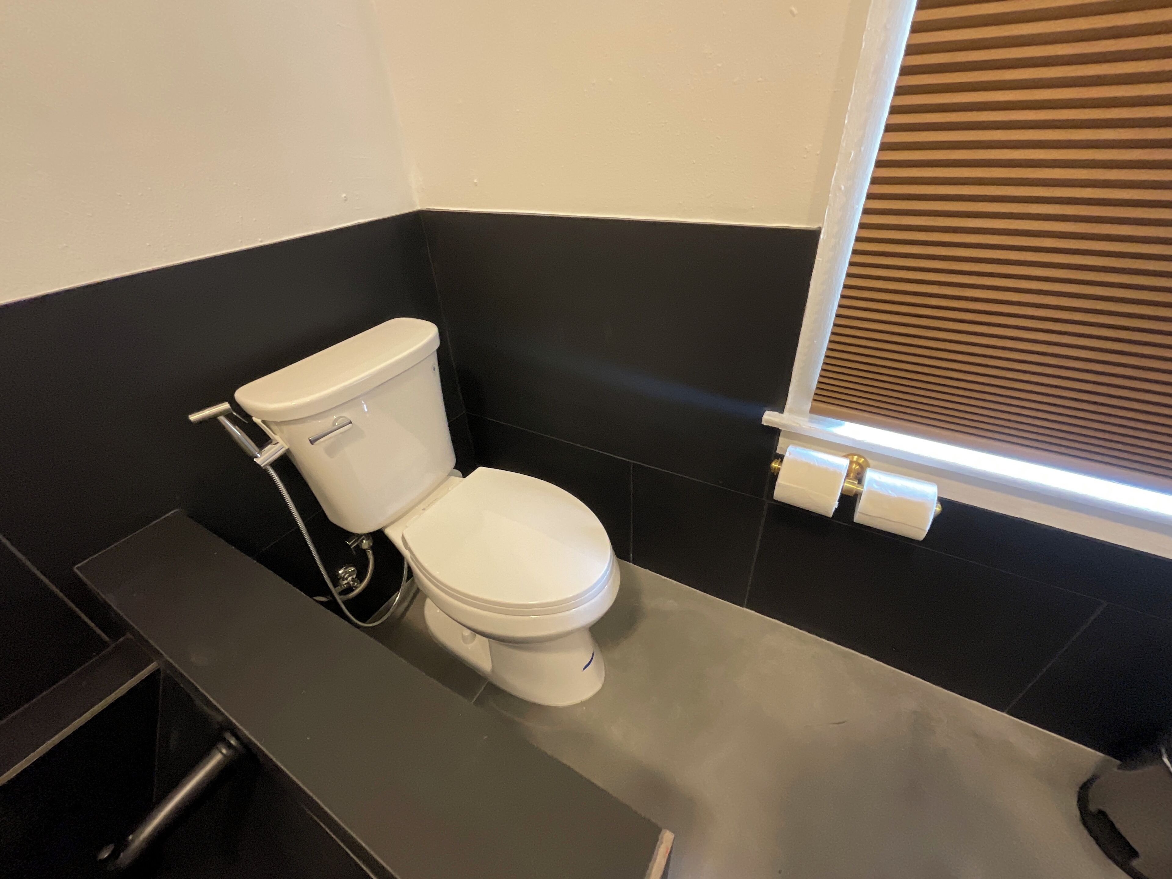 Une salle de bain avec des toilettes blanches, des murs noirs et une fenêtre avec des stores.
