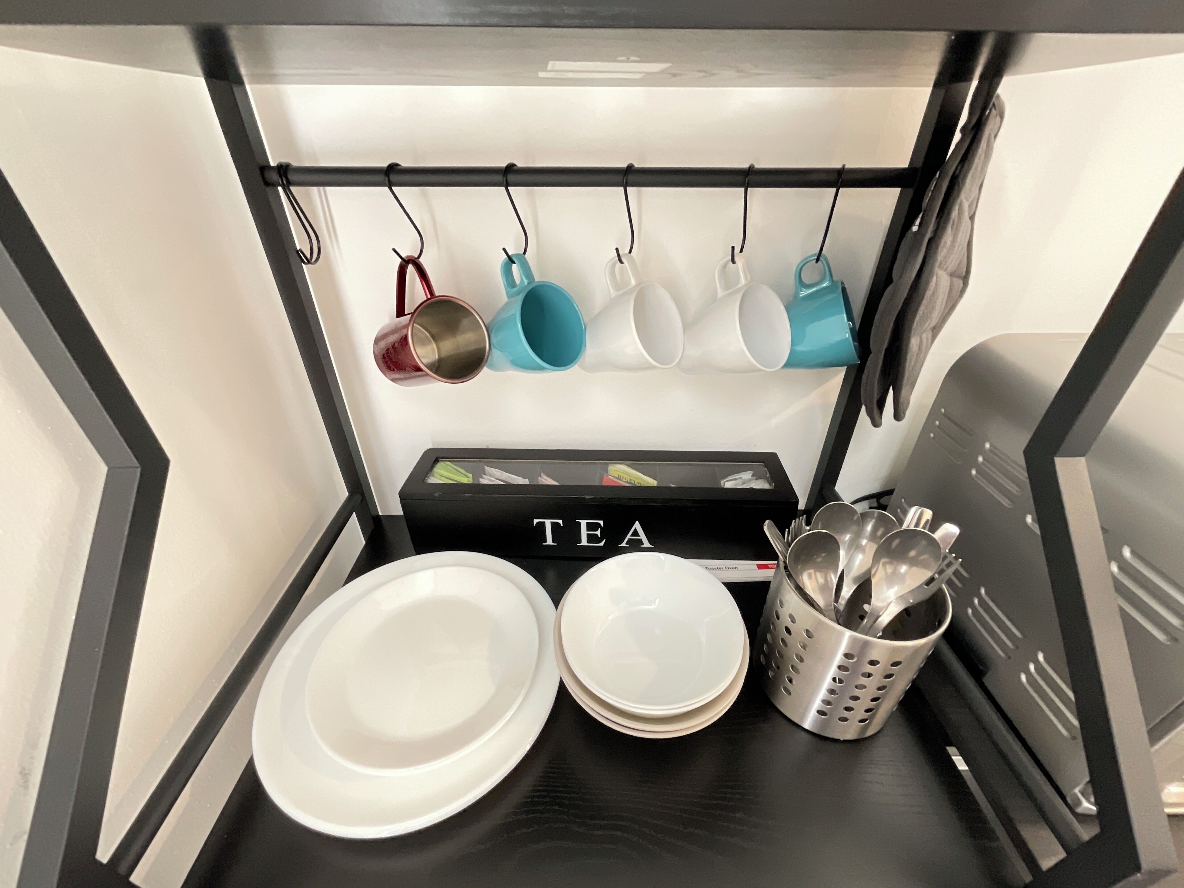A kitchen counter with a tea station, including a box labeled "TEA," a set of white plates, and a utensil holder.