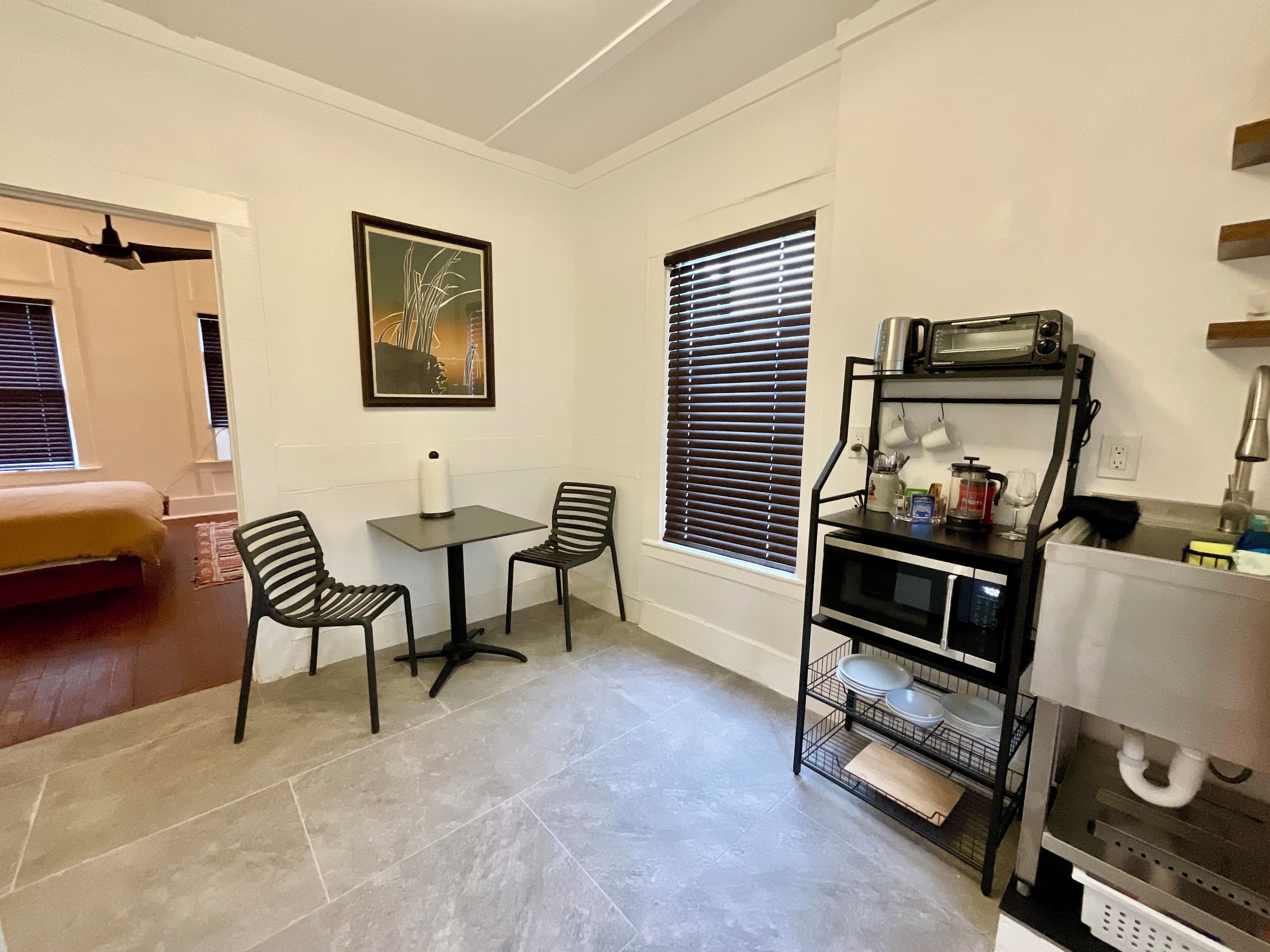 A compact kitchen with a dining area, a microwave, a coffee maker, and a shelf with dishes.