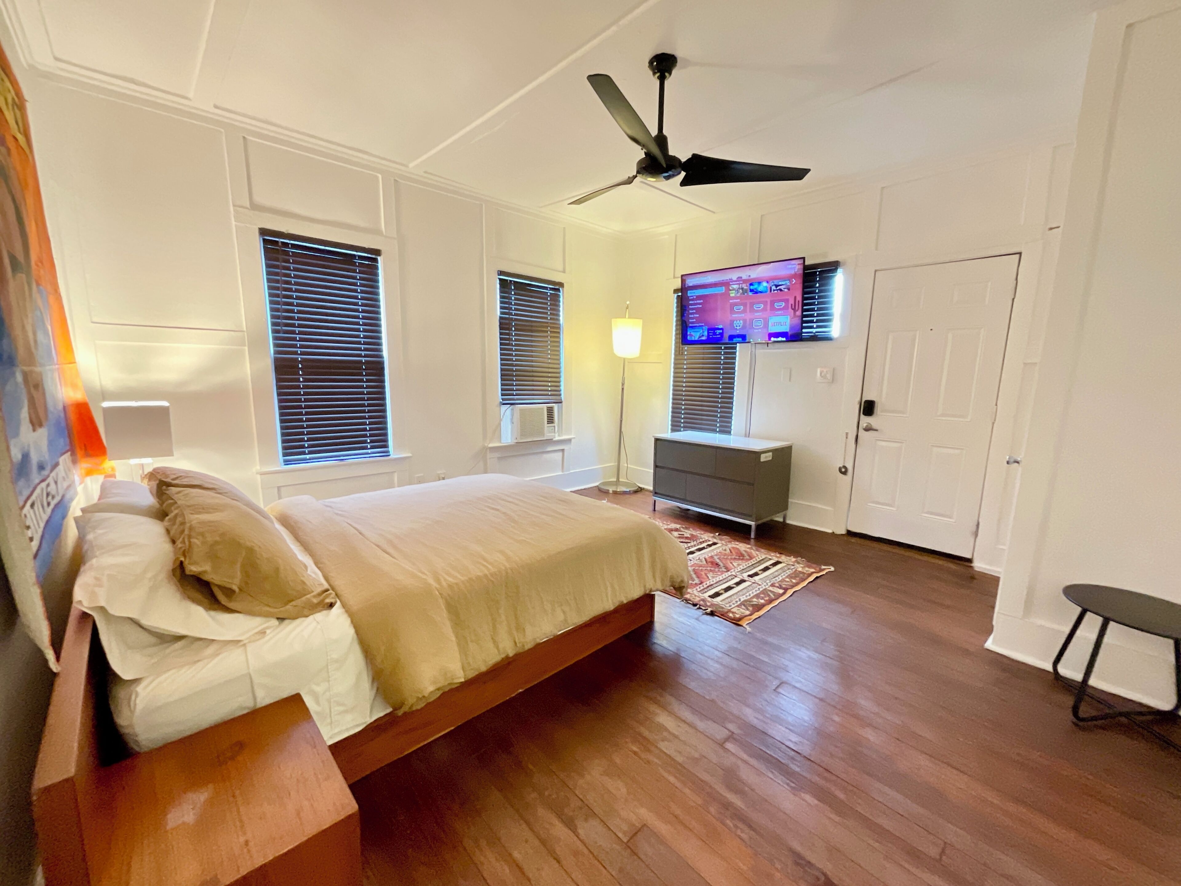 Une chambre à coucher avec un lit, un ventilateur de plafond, un téléviseur fixé au mur et une commode.