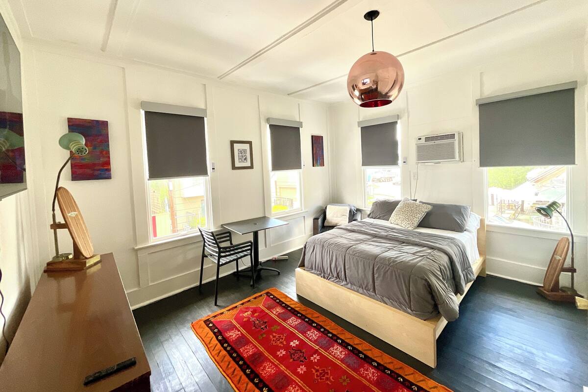 Ein Schlafzimmer mit Bett, Schreibtisch, Stuhl und einem roten Teppich mit Muster.