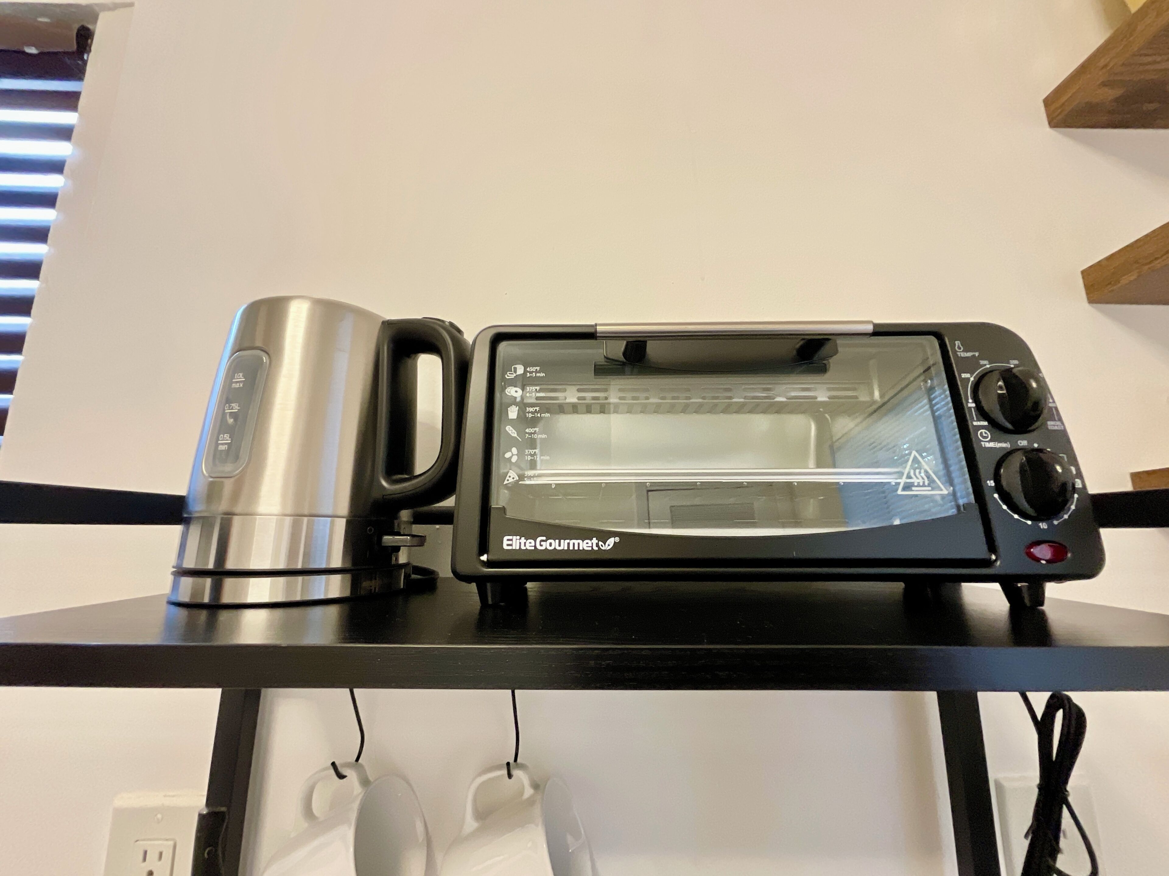 Horno tostador sobre una encimera negra, con pantalla digital, una cafetera y un enchufe.