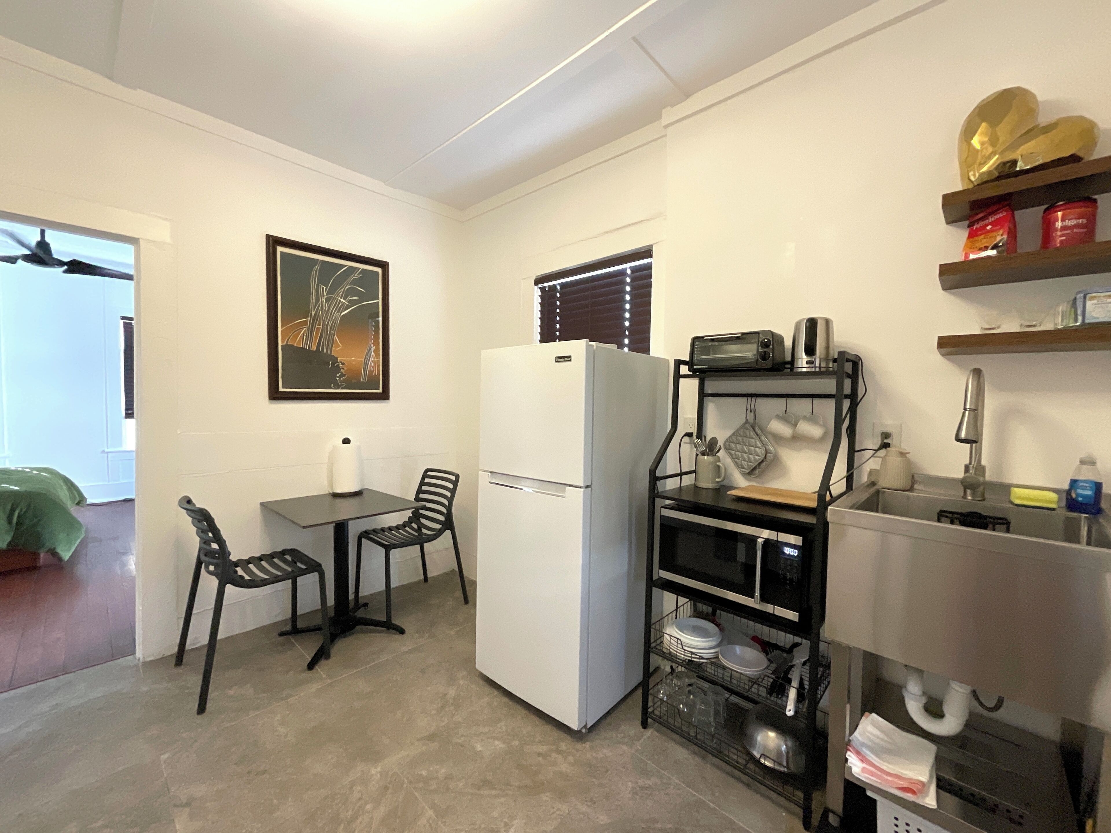 A compact kitchen with a refrigerator, a small dining table with chairs, a microwave, and a sink with a stainless steel countertop.