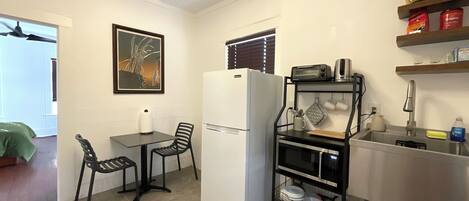 A compact kitchen with a refrigerator, a small dining table with chairs, a microwave, and a sink with a stainless steel countertop.