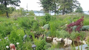 Un jardín con un estanque, diversas plantas y una estatua.