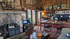 Un interior rústico con chimenea de piedra, muebles de madera y una zona de cocina con ollas colgantes.