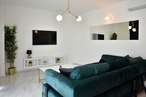 Una sala de estar moderna con un sofá verde, un televisor de pantalla plana, una consola blanca y un espejo grande.