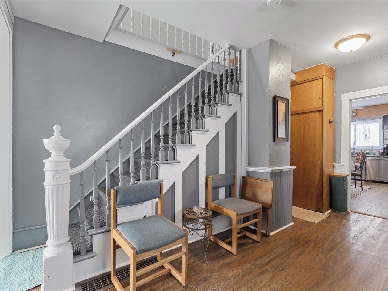 A staircase with white balusters and a wooden handrail, leading to a landing with two wooden chairs and a small table.