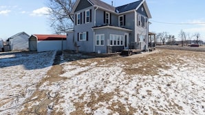 A two-story house with a red roof, a front porch, and a yard with snow patches. - Pet-friendly Historic 4BR Home in Illinois (Lynn Center)