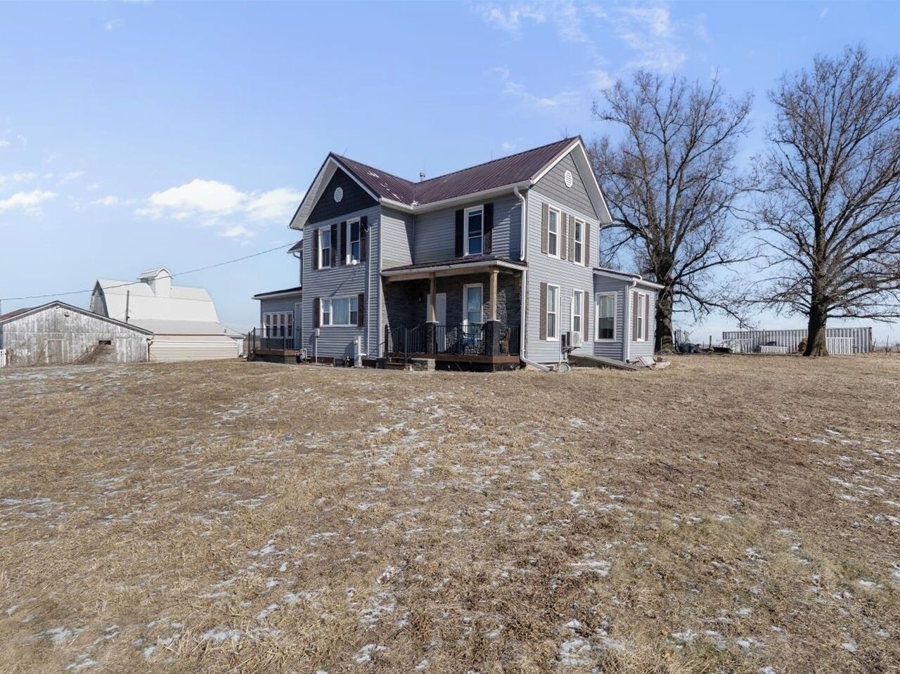A two-story house with a porch, a fenced yard, and a large tree to the right.
